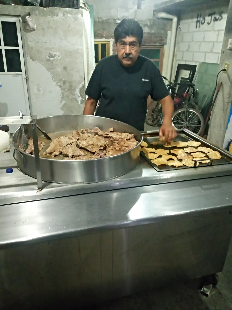 El taquero sirviendo suadero del cazo junto al comal con tortillas
