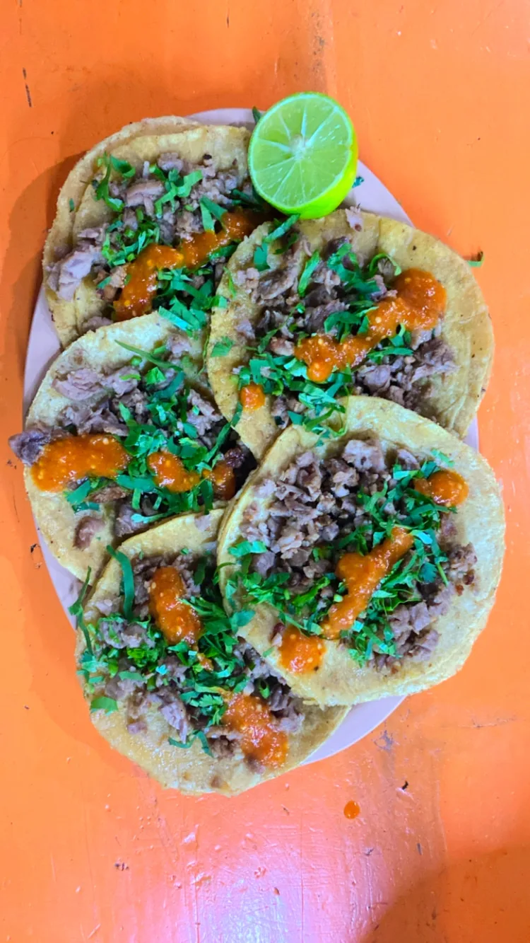 Plato de tacos de suadero con cilantro, salsa roja y limón sobre una mesa naranja